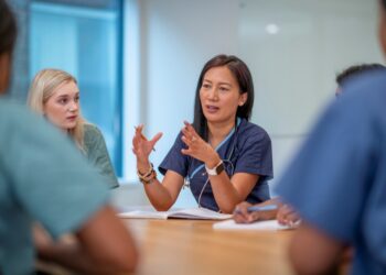 A person in a blue scrubs talking to a group of people Description automatically generated with low confidence